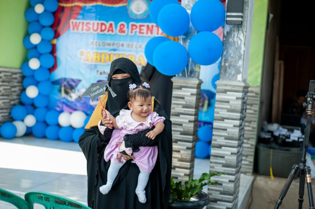 A mother in traditional clothing holds her baby at a festive event with balloons.