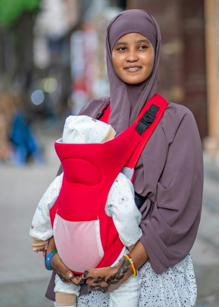 A smiling Somali mother holds her baby in a red carrier on a street in Mogadishu, Somalia.