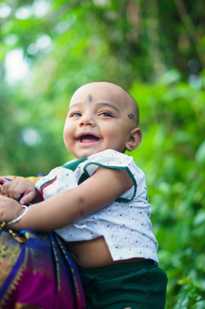 Smiling South Asian baby boy enjoying outdoor nature scene in Howrah, India.