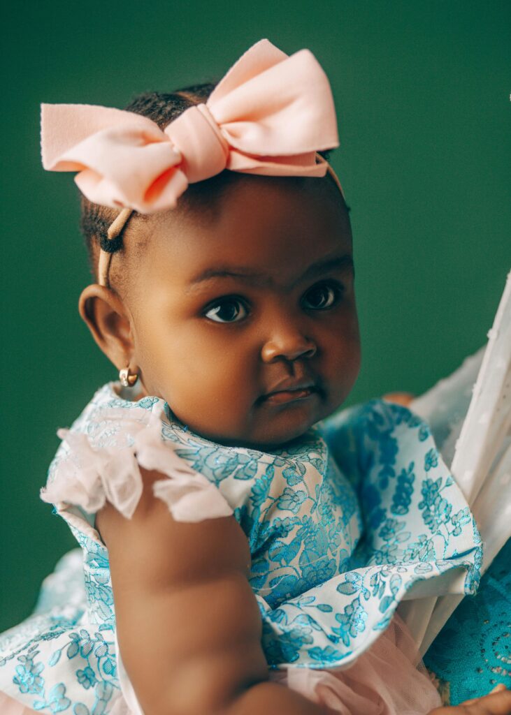Adorable baby girl wearing a pink bow and floral dress in portrait.