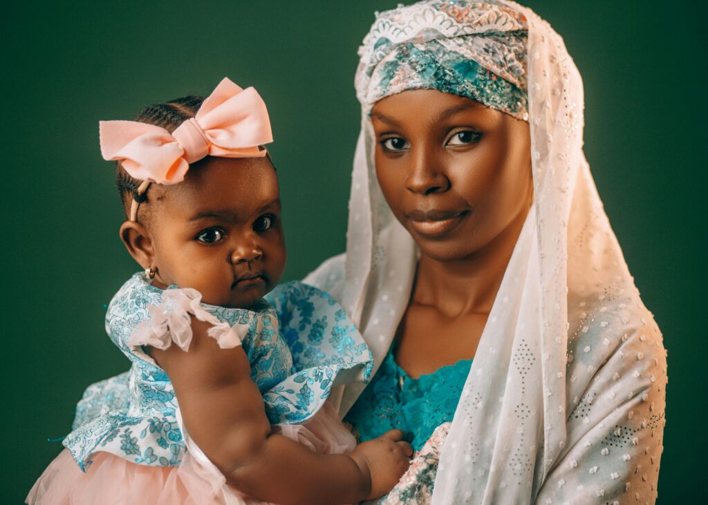 A mother lovingly holds her baby, both dressed in vibrant traditional Nigerian attire.
